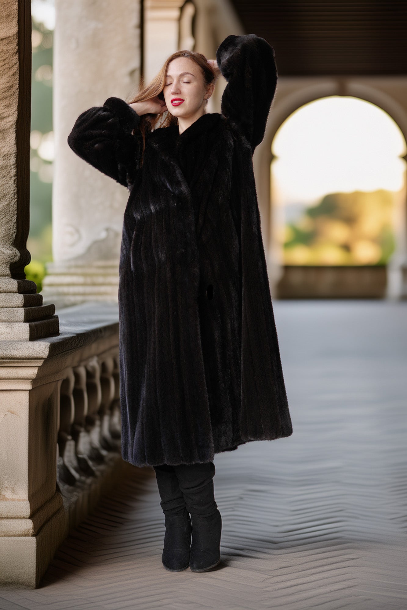 Woman wearing a long black coat standing in an outdoor setting with columns and arches.