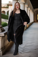 Woman in a black coat standing in an outdoor setting with columns in the background