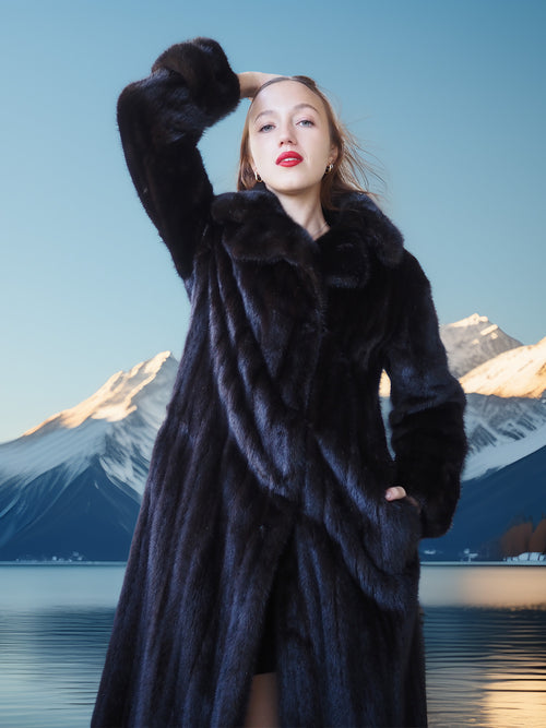 Woman in a fur coat standing in front of mountains and water