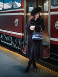 Woman in a fur coat and hat holding a handbag at a train station.