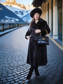 Woman in a black coat and hat holding a black handbag on a snowy mountain street.