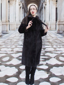 Model wearing La Galleria full-length mahogany mink fur coat with tie closure, styled in a grand architectural setting for winter fashion.