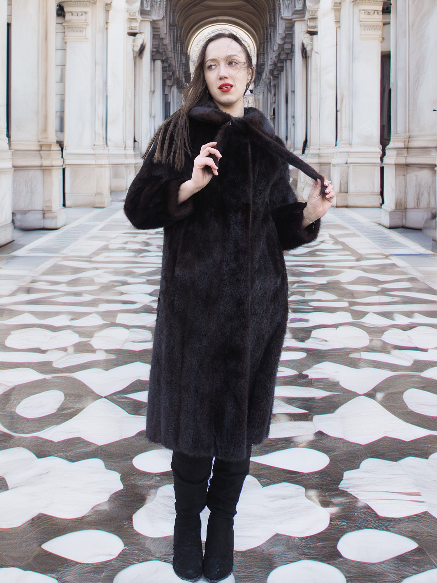 Model wearing La Galleria full-length mahogany mink fur coat with tie closure, styled in a grand architectural setting for winter fashion.