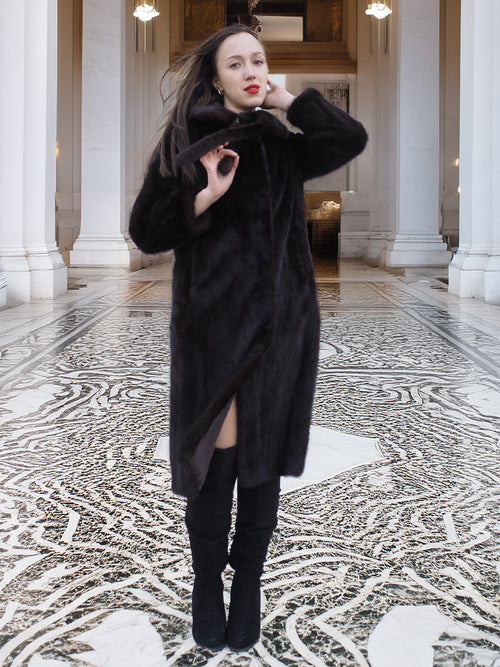 Model posing in La Galleria mahogany mink fur coat with tie-front, styled for elegant winter fashion in a grand architectural setting.