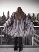 Person wearing a fur coat standing on a rooftop with city skyline view