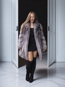 Woman wearing a fur coat and black boots standing in an open doorway.
