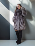 Woman wearing a fur coat standing against a plain wall.
