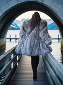 Person wearing a fur coat walking on a bridge with a scenic background