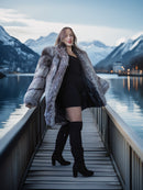 Woman in a fur coat standing on a dock with mountains and water in the background
