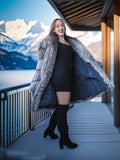 Woman in a fur coat standing on a balcony with a mountain view