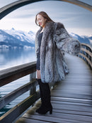 Woman in a fur coat standing on a wooden dock with mountains in the background