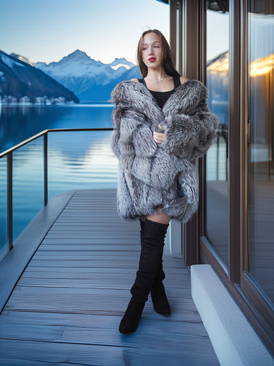 Woman in a fur coat standing on a dock with mountains and water in the background
