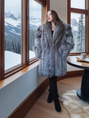 Woman in a fur coat standing by a window with snowy mountain views