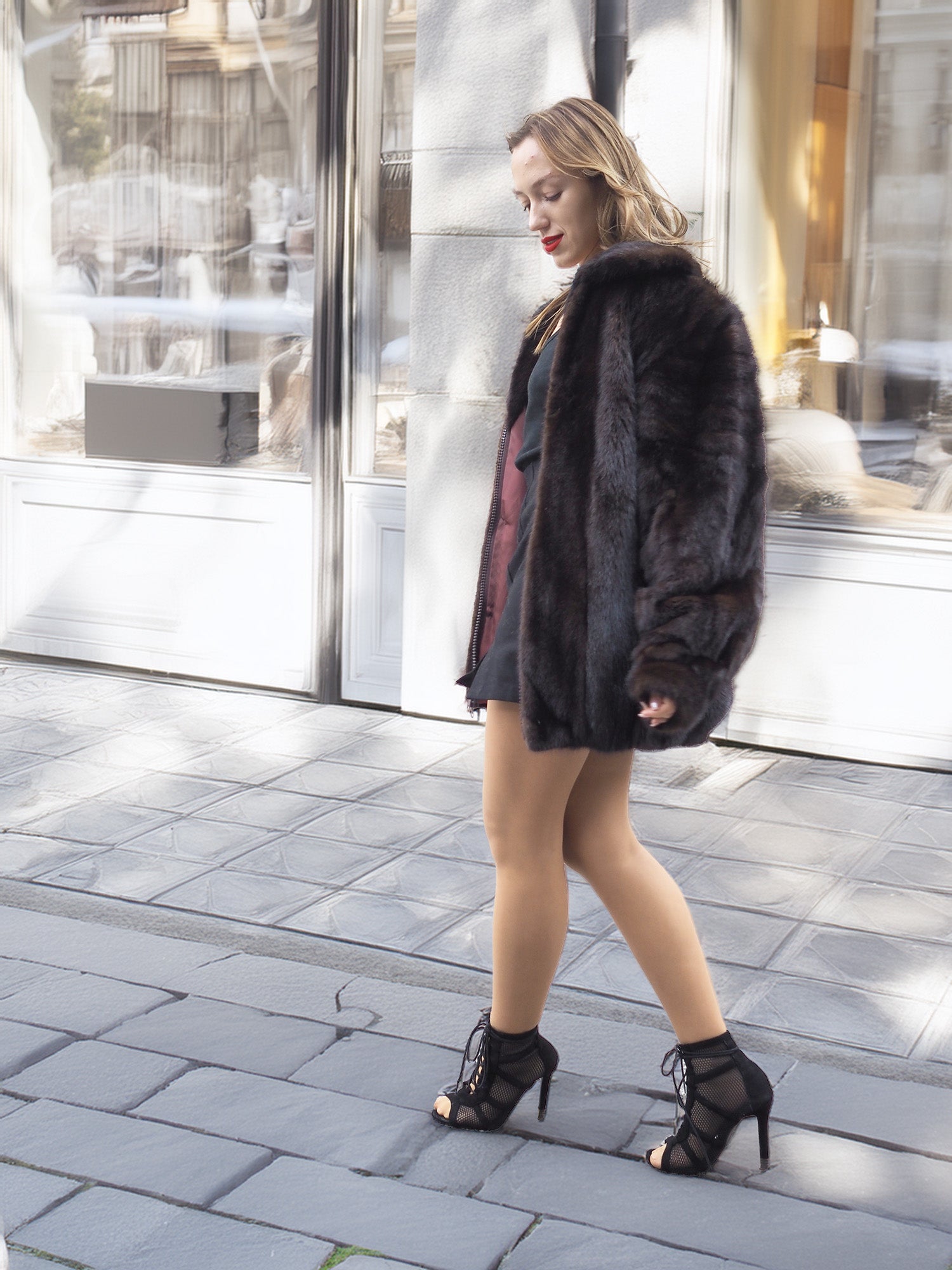 Model walks past storefronts in Unisex Dark Mahogany Mink Fur Bomber Jacket Coat M/L, highlighting its elegant cut and satin lining.