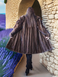 Person wearing a fur coat standing in front of a stone wall with lavender fields in the background