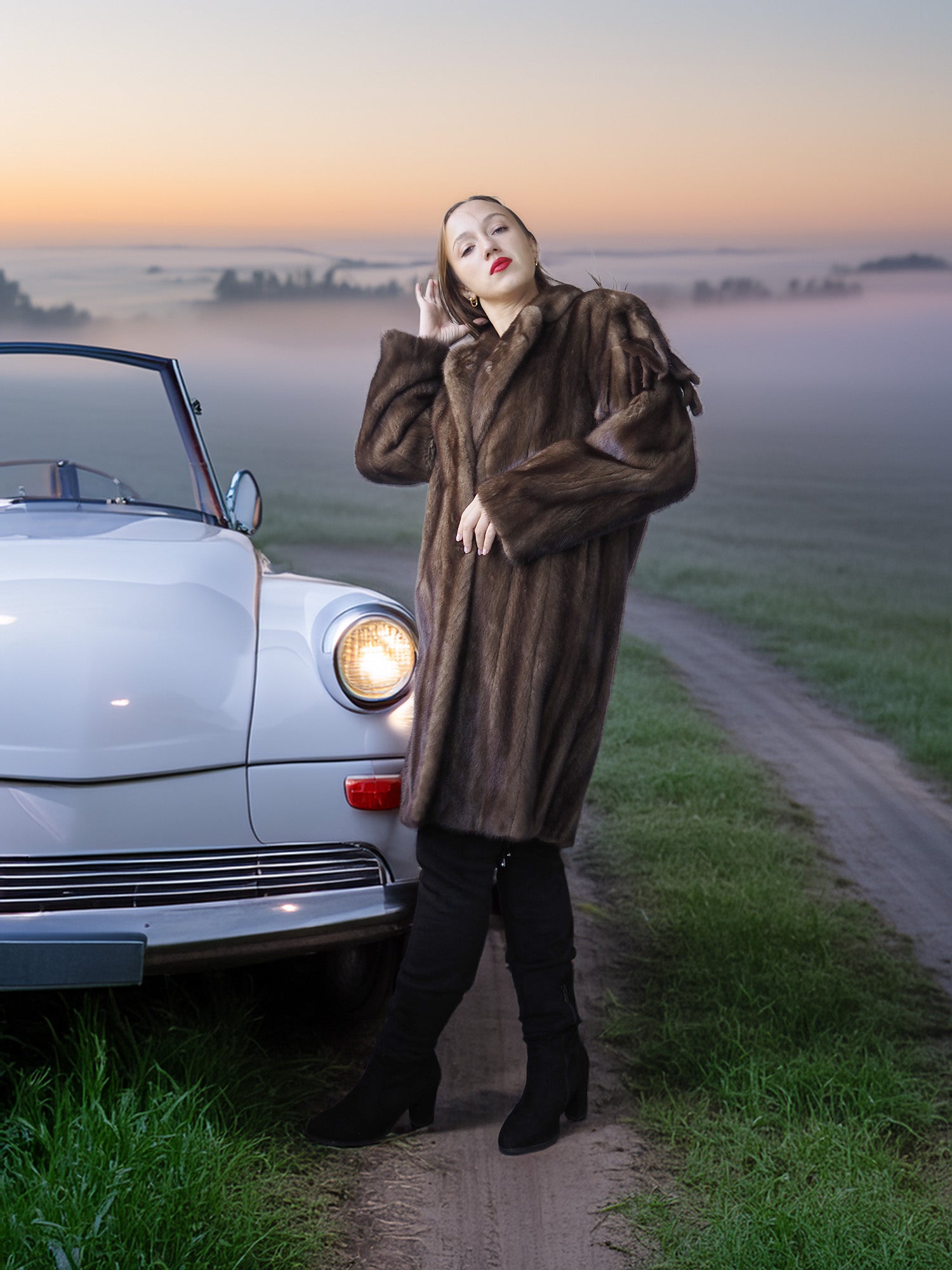 Woman in a fur coat standing next to a vintage car on a foggy road.
