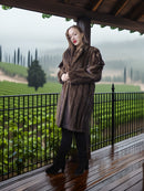 Woman in a brown fur coat standing on a wooden deck with vineyard view
