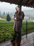 Woman in a brown fur coat standing on a wooden deck with vineyard view