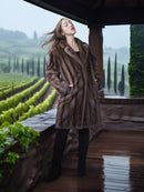 Woman in a fur coat standing on a wooden deck with vineyards in the background