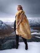 Person wearing a fur vest standing in a snowy landscape with mountains.