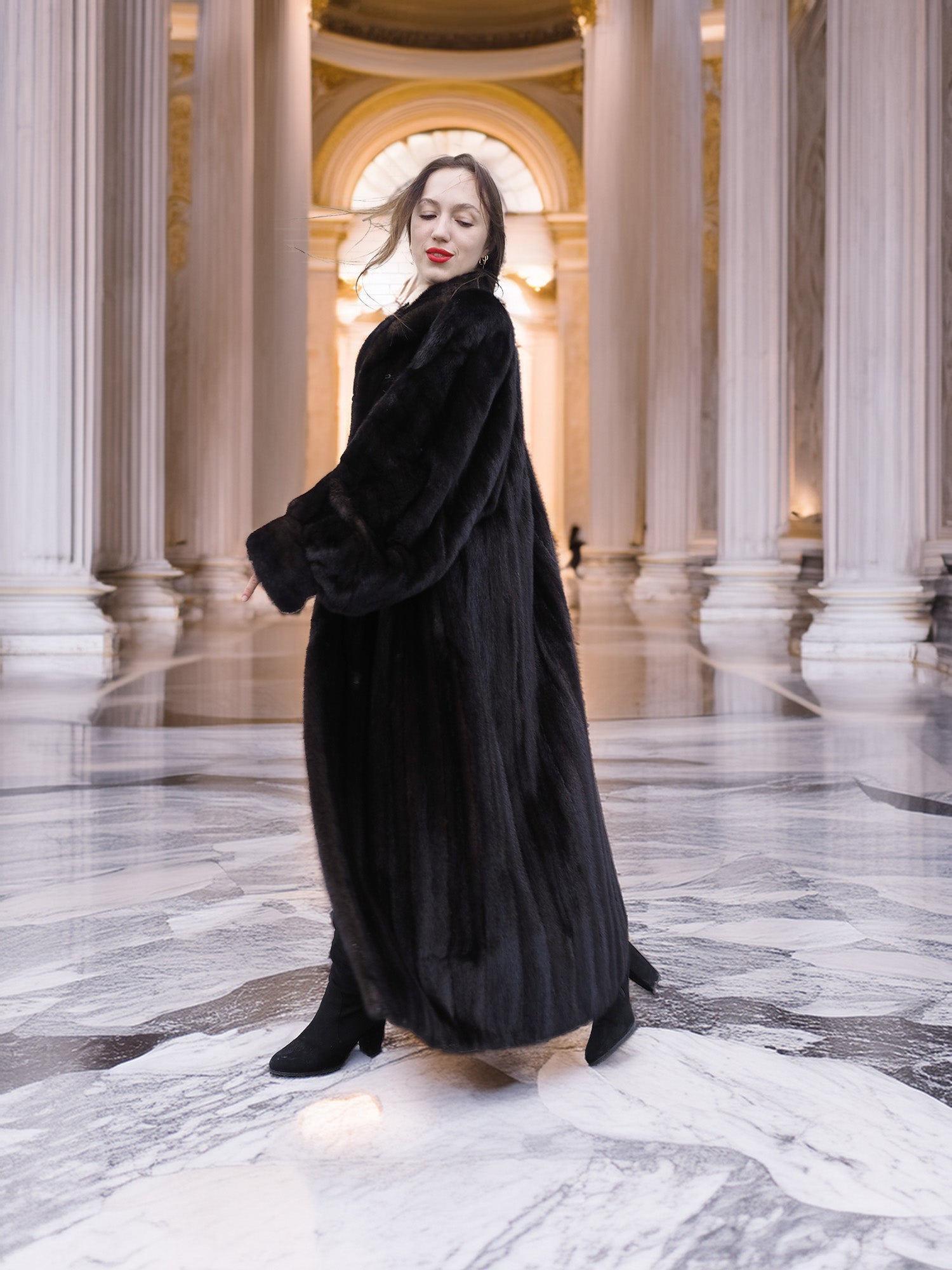 Black mink coat flows gracefully in a marble hall, capturing the essence of opulent winter fashion and timeless fur apparel.