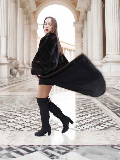 Black mink coat flares in motion, styled with thigh-high boots for a chic and dramatic winter outerwear look.