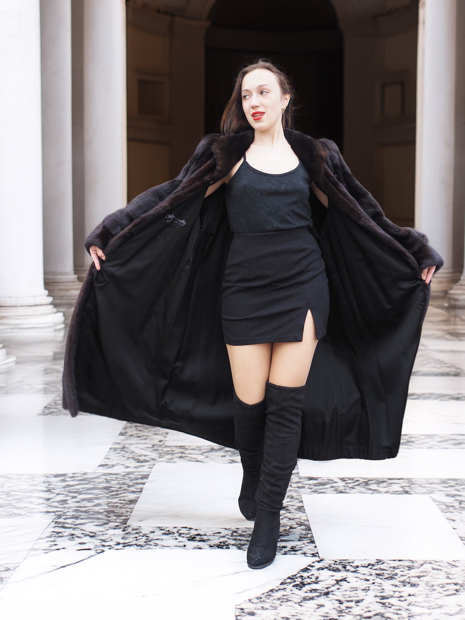 Model opens black mink coat to reveal black mini dress, combining bold fashion with luxury fur outerwear appeal.
