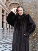 Smiling model leans against marble column in black mink coat, highlighting plush texture and timeless fur fashion appeal.
