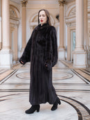Model walks confidently in full-length black mink coat, styled for upscale winter fashion in a neoclassical setting.