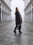 Smiling model in black mink coat with indigo fox trim, walking confidently through a cobblestone street in winter fashion.