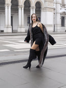 Model in black mink coat with indigo fox trim, walking confidently in a city square, styled with black boots.