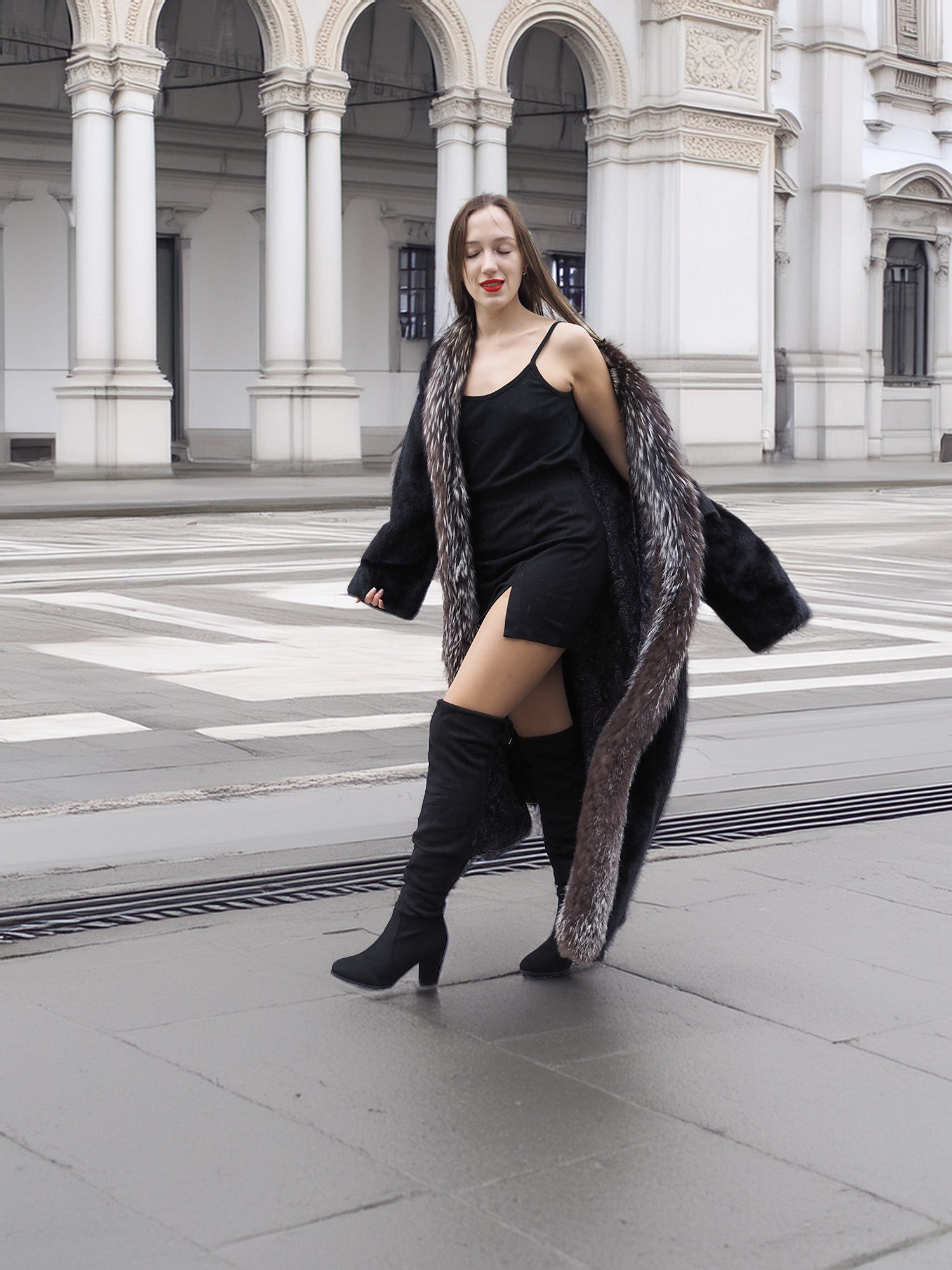 Model in black mink coat with indigo fox trim, walking confidently in a city square, styled with black boots.