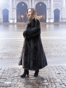 Side view of black mink coat with indigo fox collar, styled with black boots for a refined winter fashion statement.