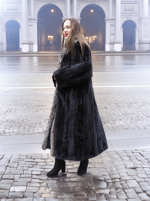 Side view of black mink coat with indigo fox collar, styled with black boots for a refined winter fashion statement.