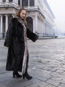 Side view of black mink coat with silver fox trim, styled for a chic winter look in a foggy urban setting.