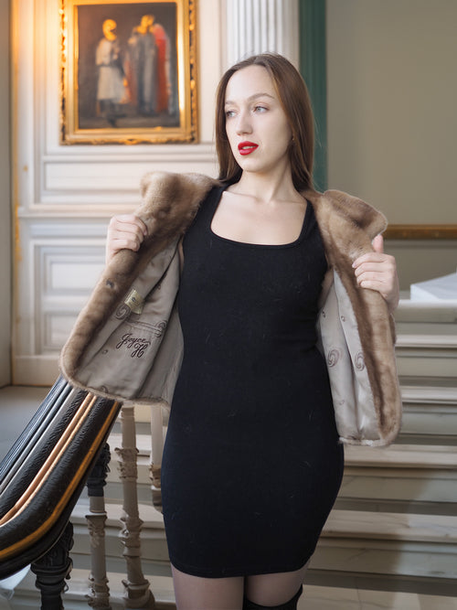 Woman wearing a black dress and fur coat in an elegant interior setting