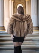 Person wearing a fur coat standing on steps with classical architecture in the background
