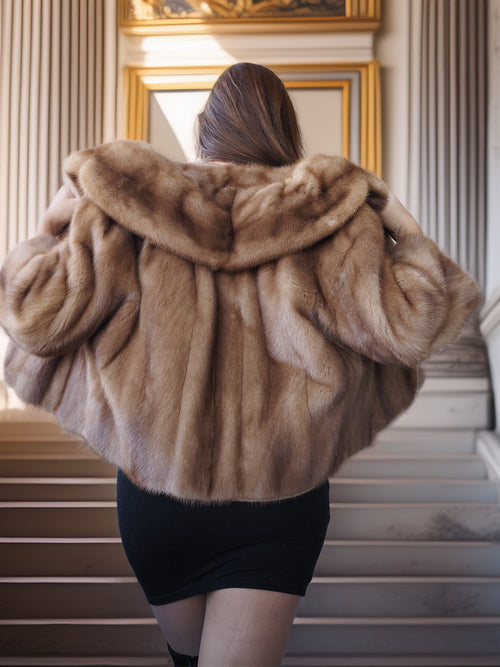 Person wearing a fur coat standing on a staircase with ornate walls.