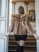 Person wearing a fur coat standing in a doorway with classical architecture.