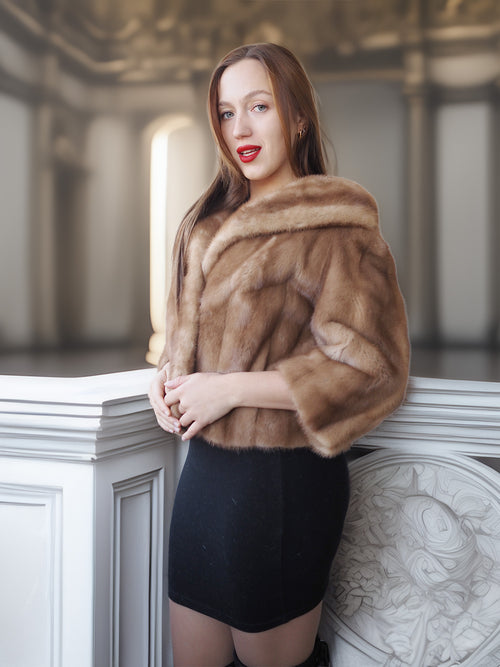 Woman wearing a brown fur coat standing against a decorative wall.