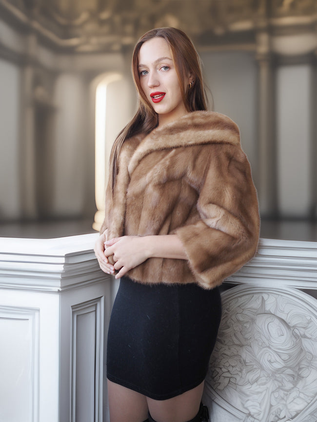 Woman wearing a brown fur coat standing against a decorative wall.