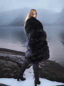 Woman in a fur coat standing on a snowy log by a body of water
