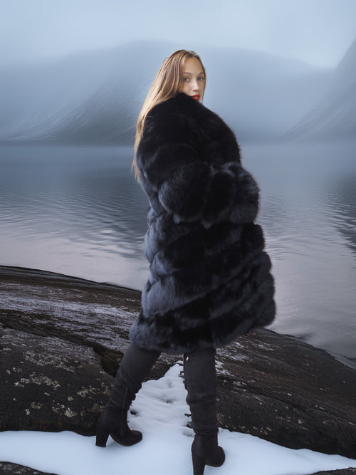 Woman in a fur coat standing on a snowy log by a body of water