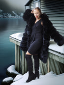 Woman in a black fur coat and dress standing on a snowy dock.