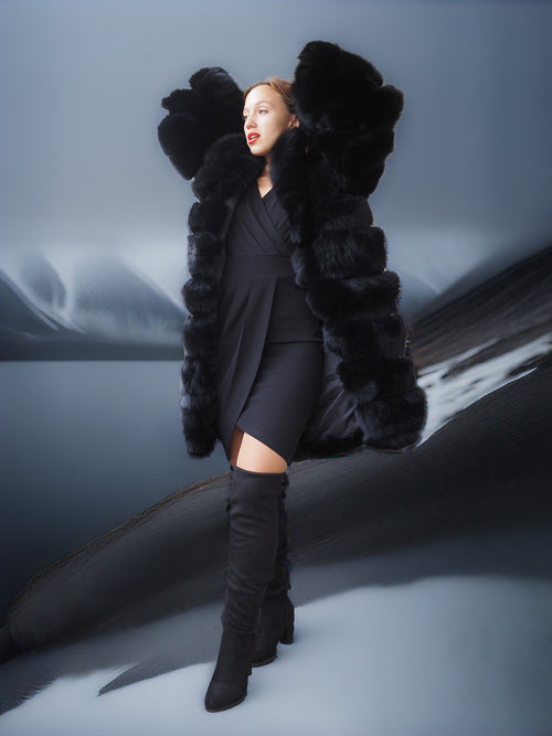Person wearing a black fur coat and knee-high boots in a snowy landscape