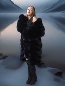 Woman in a black fur coat standing on a snowy landscape with mountains in the background