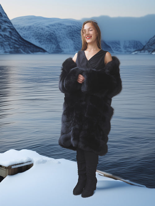 Woman in a black fur coat standing on a snowy landscape with mountains in the background