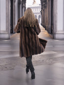 Back view of woman walking in dark mahogany mink fur coat, emphasizing the coat's full length and premium fur quality.