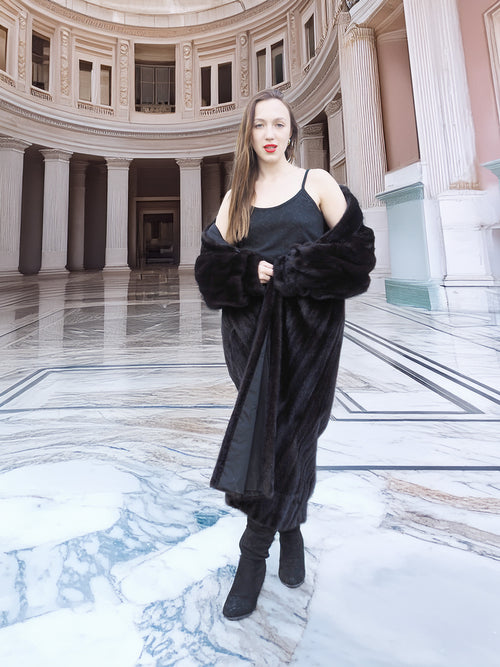 Model in black mink fur coat with one shoulder exposed, styled in a grand rotunda. Full-length fur outerwear, size M.