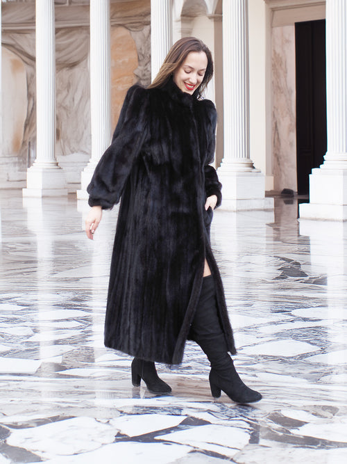 Model walking in black mink fur coat with front slit, paired with black boots. Full-length luxury fur outerwear, size M.